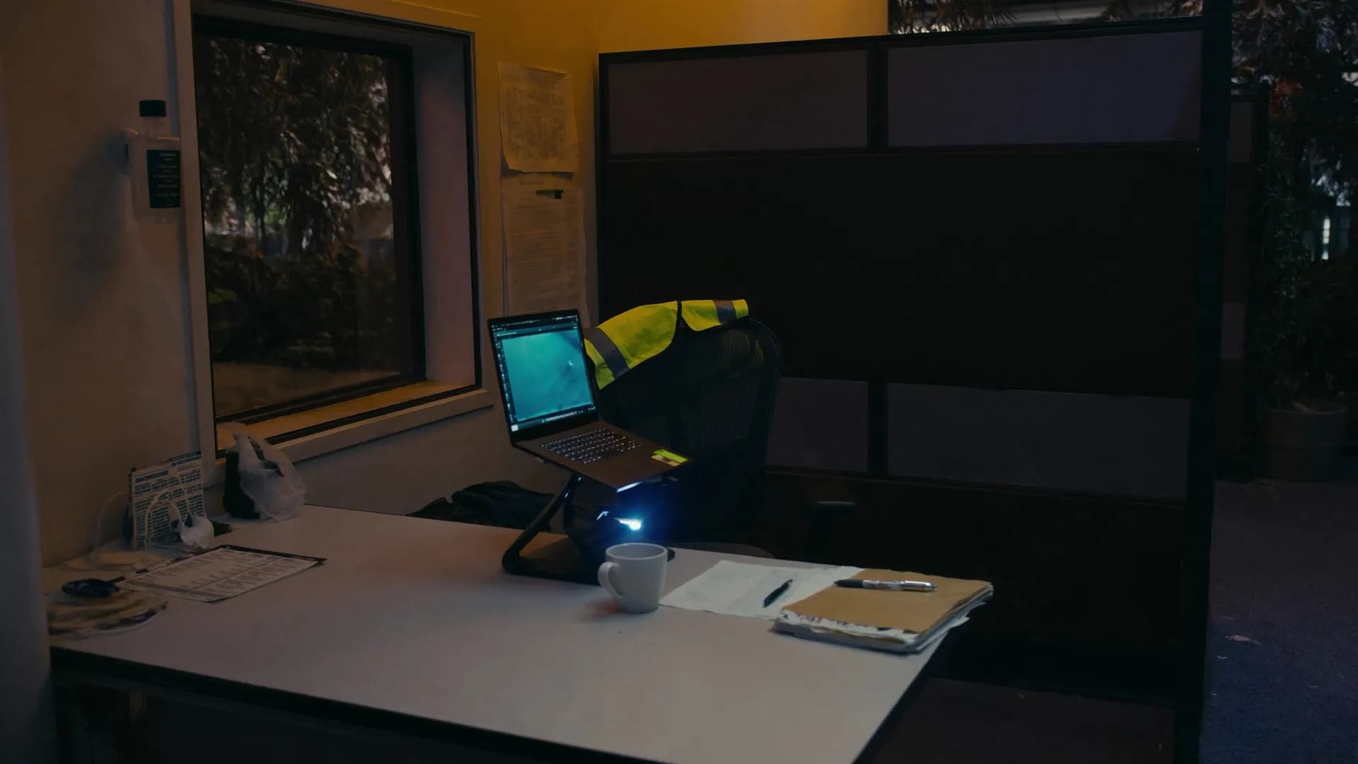 A small founder-run workspace with a laptop and a hi-vis vest on the chair